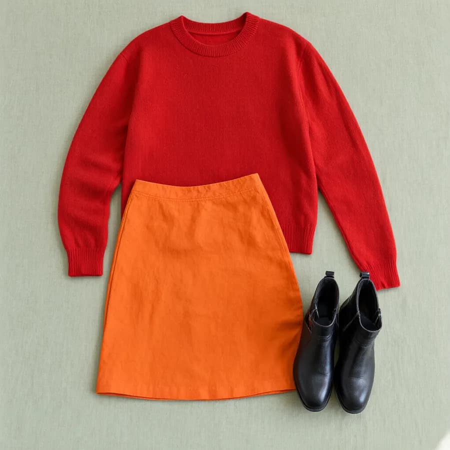 A flat lay of red sweater, orange skirt and black boots
